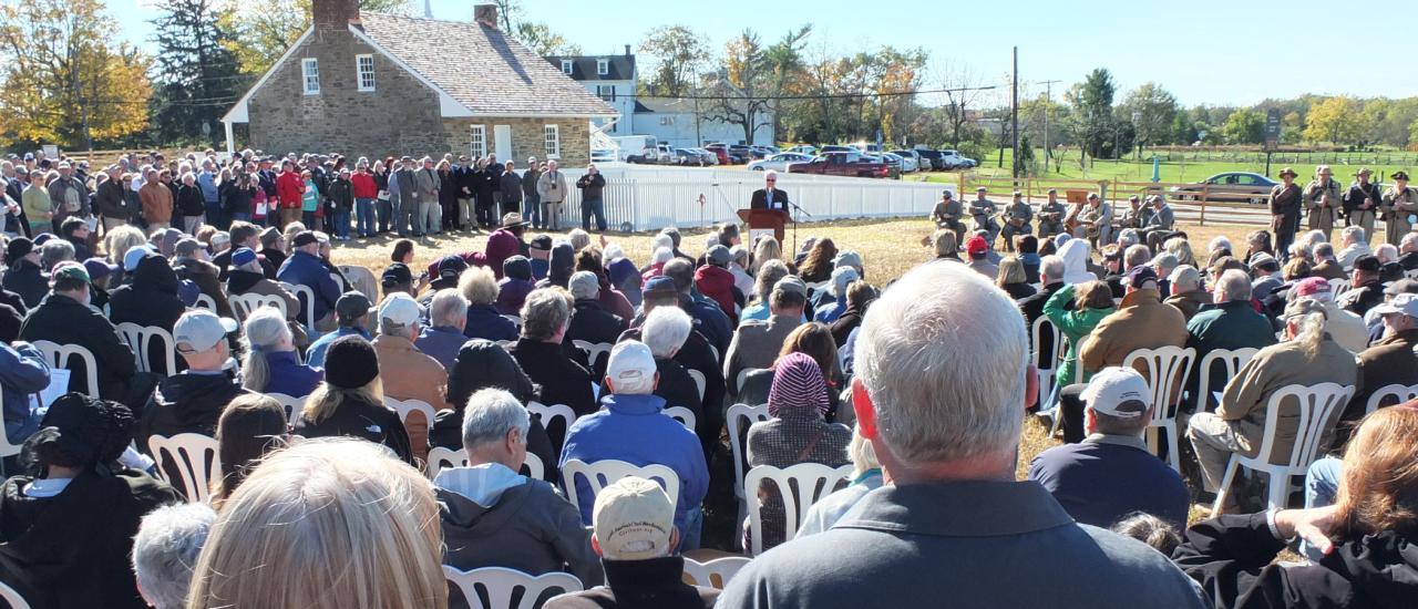 A large crowd gathers outside in front of the building of historic Mary Thompson house, a speaker is seen at the podium to make an announcement