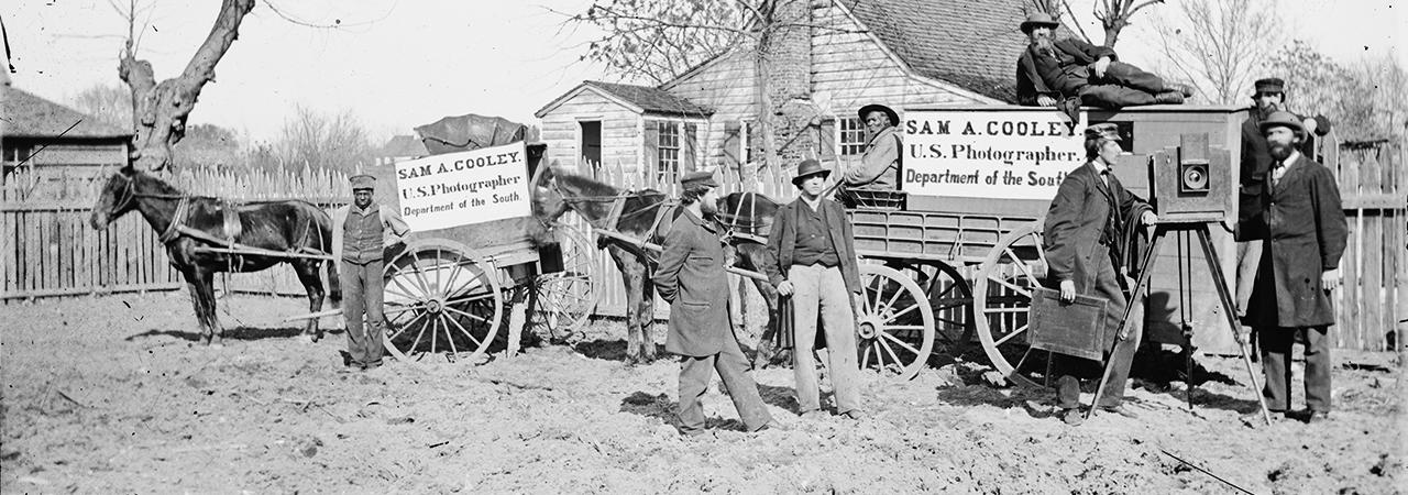 A black and white photograph of men advertising with signs posted on their horse and buggies