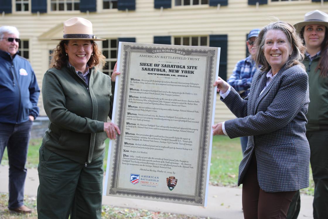 Leslie M. Morlock, Superintendent of Saratoga National Historical Park, and Kathy Robertson, Director of Project Management at the American Battlefield Trust, hold the ceremonial deed.